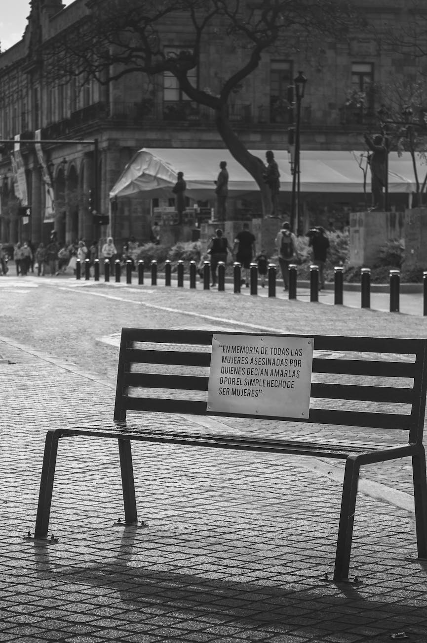 grayscale photo of bench with people walking on street